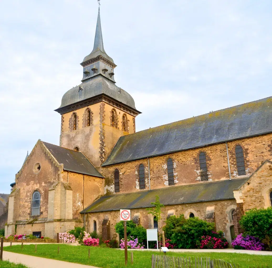 L'église abbatiale de Saint-Gildas-des-Bois, son clocher et ses murs en grès roussard, vue depuis le jardin fleuri